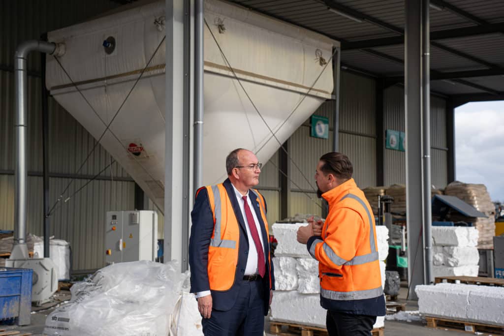 Photo de Philippe Deschamps, Sous-Préfet de Thionville, et Quentin Ehlinger, directeur général du groupe VALO' qui discute devant le broyeur-compresseur à polystyrène du site d'exploitation de tri des déchets Triplast.