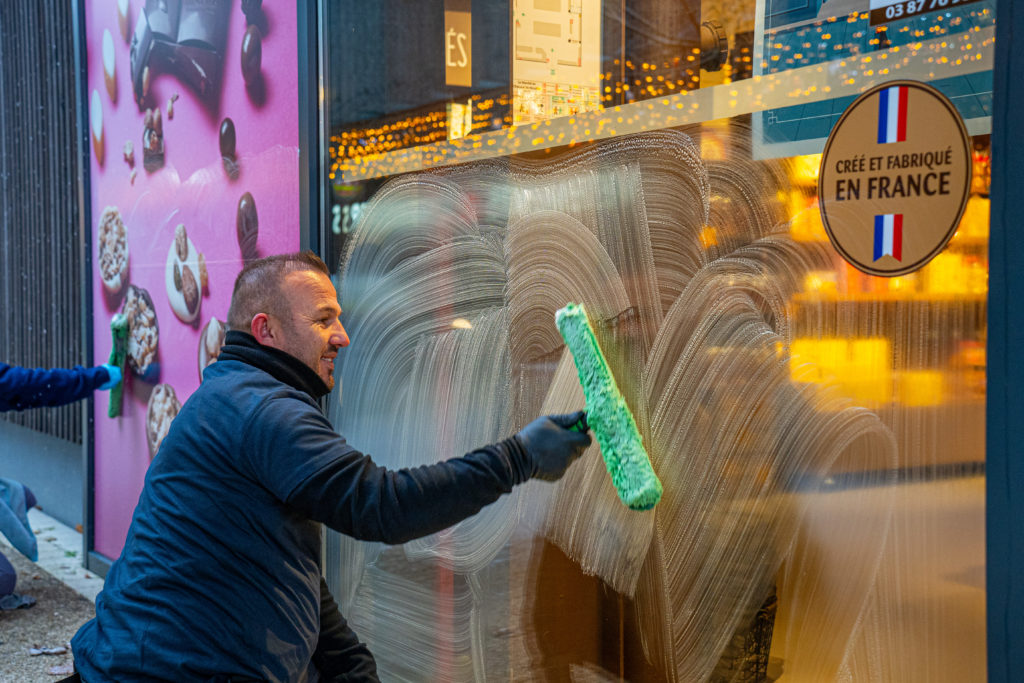 Photo de Shukri Ismajli, chef d'équipe vitrerie pour VALO'Propreté, en train de nettoyer la vitrine commerciale du marché au chocolat de Neuville, situé au SuperGreen à Terville.